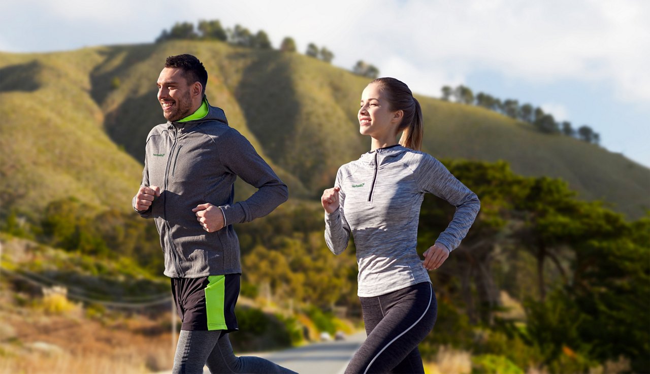 A man and woman running outdoors A man and woman running outdoors, wearing Herbalife branded apparel