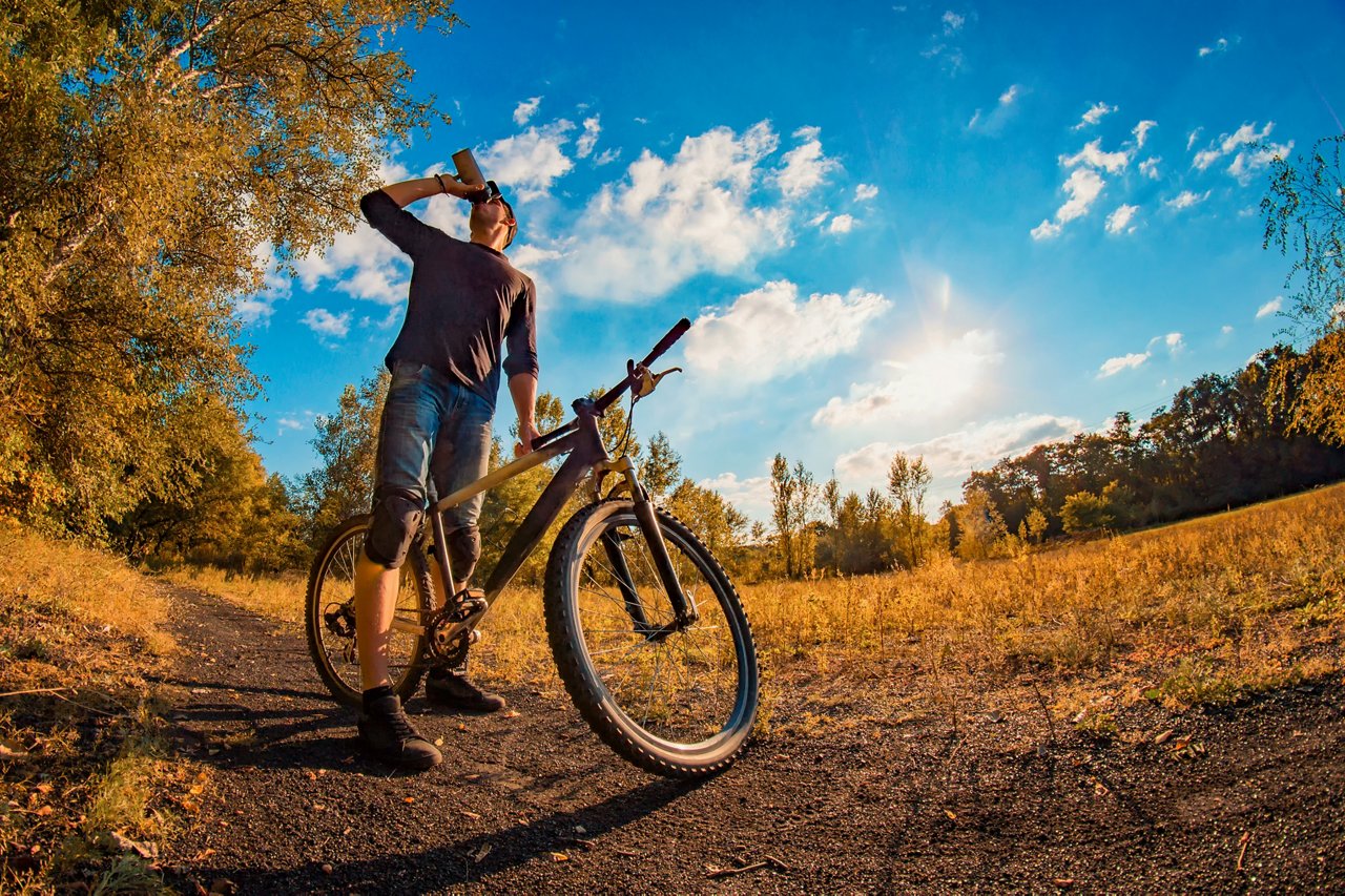 A young man drinks a protein shake from a shaker while taking a bike outdoors in the fall. A young man drinks a protein shake from a shaker while taking a bike outdoors in the fall.