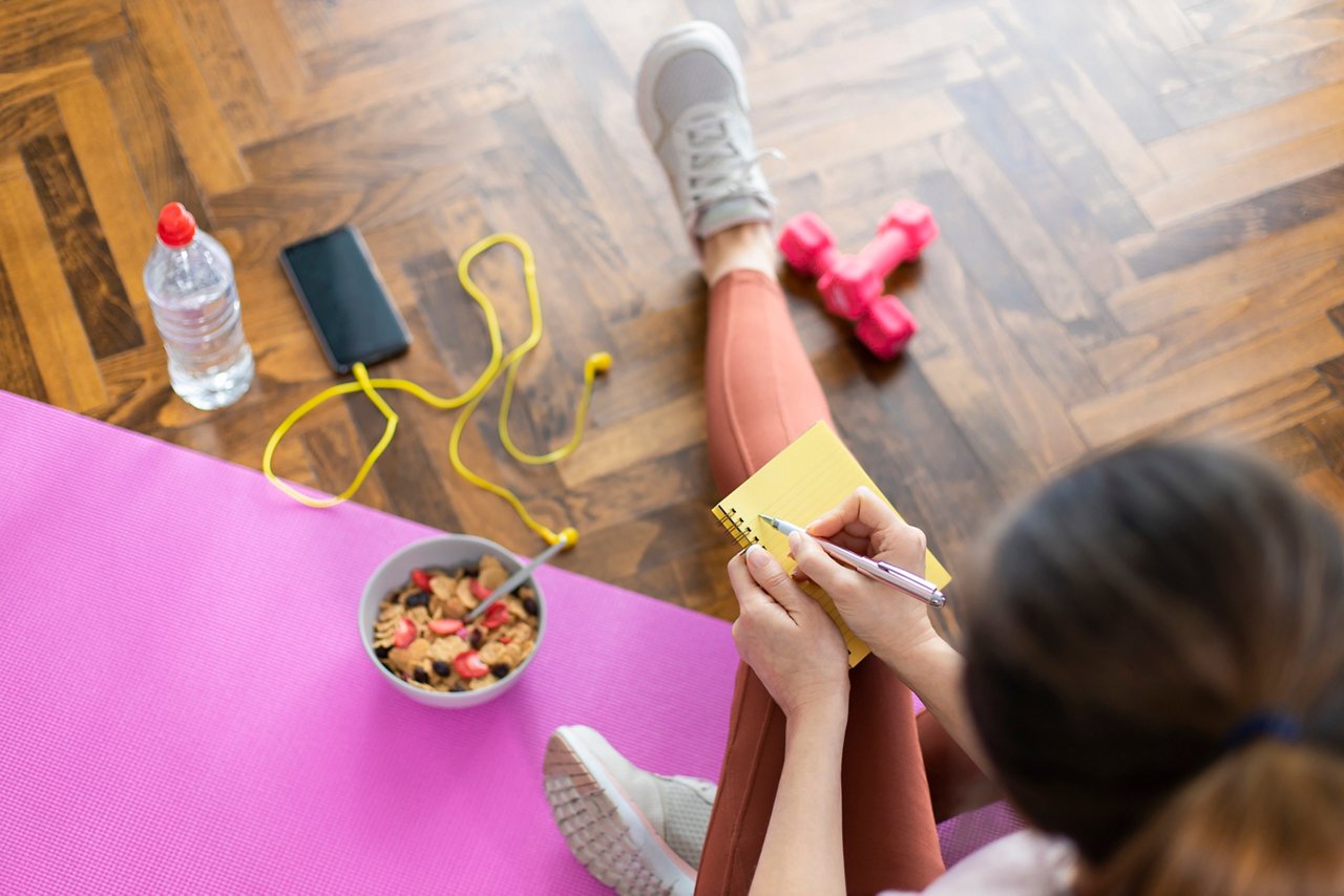 Una mujer deportista escribe en su diario de fitness para trabajar en sus propósitos de Año Nuevo. A sporty woman writing in her fitness journal to work on her New Year's resolutions