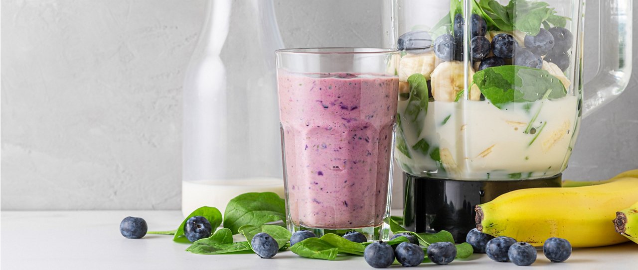 A glass of blueberry, banana and spinach protein shake with fresh ingredients in a blender A glass of blueberry, banana and spinach protein shake with fresh ingredients in a blender