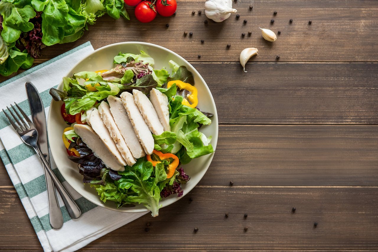 Chicken with salad on a plate with cutlery Healthy food, ready to eat mix fresh vegetable salad with skinless boiled chicken breast, top view on wood table background  with copy space