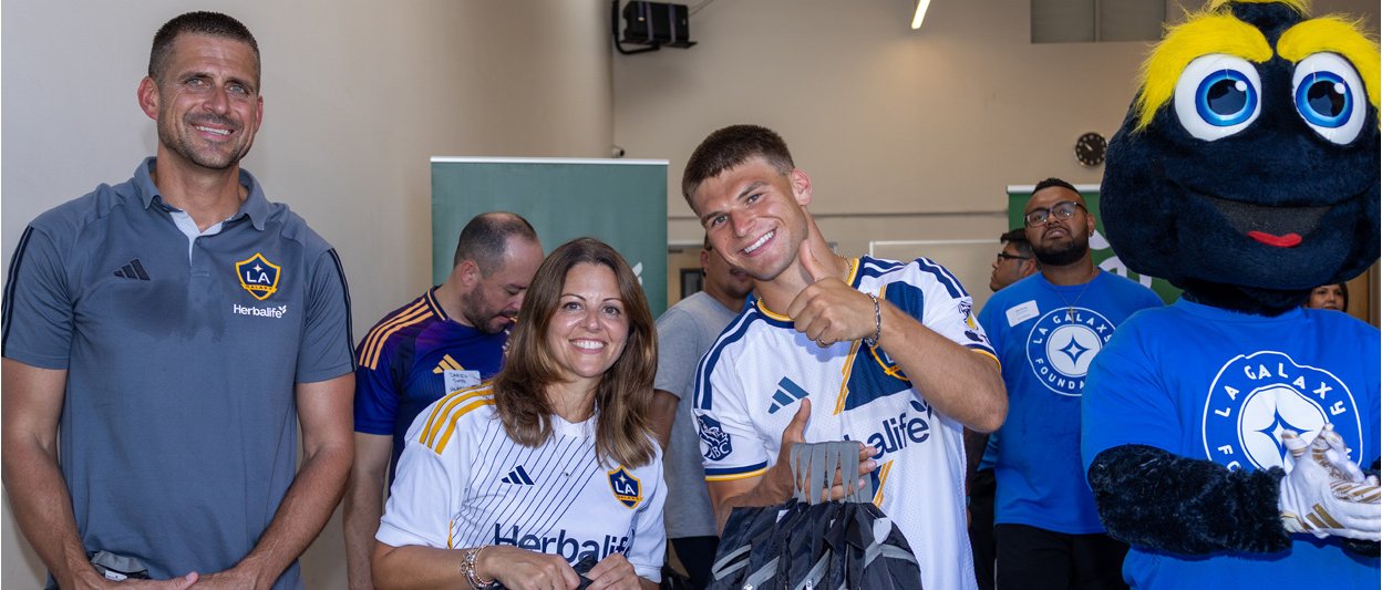 Herbalife Chief Marketing Officer Hanan Wajih, LA Galaxy players and LA Galaxy mascot Cozmo help prepare backpacks during APCH's Back-to-School Backpack Distribution in Los Angeles, supporting South Los Angeles students and families ahead of the new school year.
