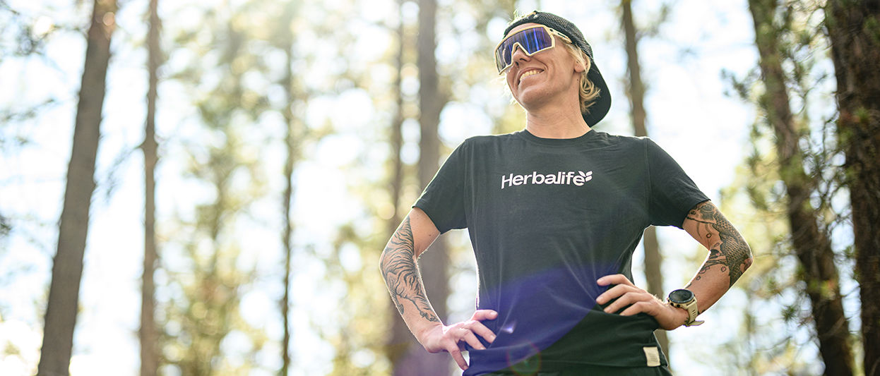 Heather Jackson, elite endurance athlete and Herbalife-sponsored runner, stands outdoors in running gear and hydration vest, looking focused before a trail run.