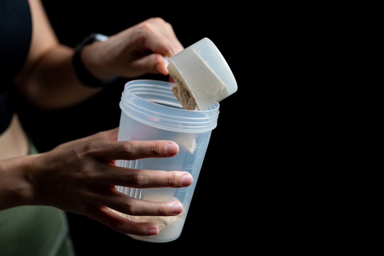 Close up of women with measuring scoop of whey protein and shaker bottle, preparing protein shake. A woman making a protein shake